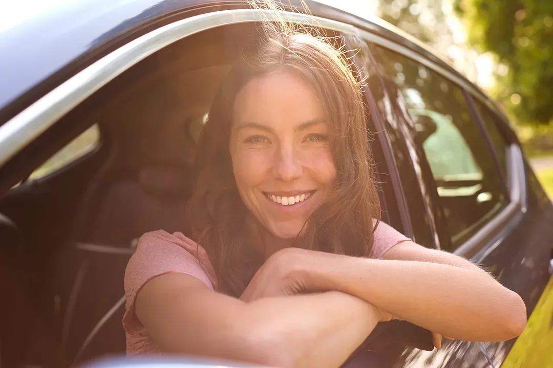 A smiling driver resting her arm on the car door